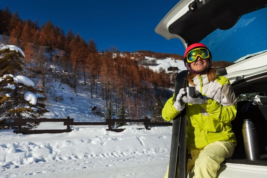 Wanita muda yang bahagia beristirahat setelah bermain ski duduk di bagasi mobil terbuka