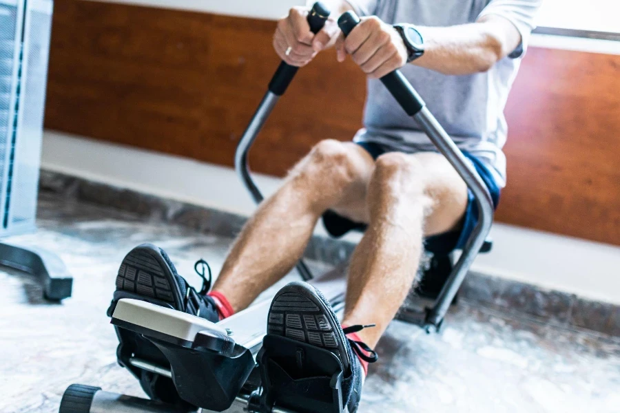 El hombre está usando una máquina de remo en el gimnasio.