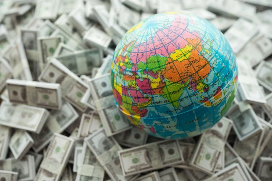 Globe on US dollar bill banknotes pile background.
