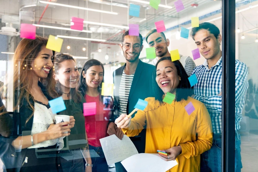 Young professionals planning tasks on glass wall with adhesive notes in co-working office