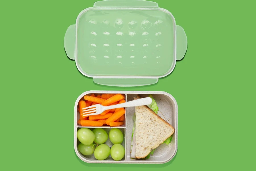 A lunch box with cutlery, grapes, carrot, and bread