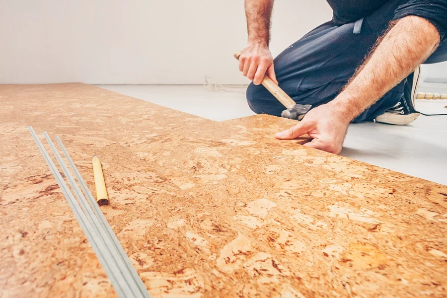 A man installing cork flooring using a hammer