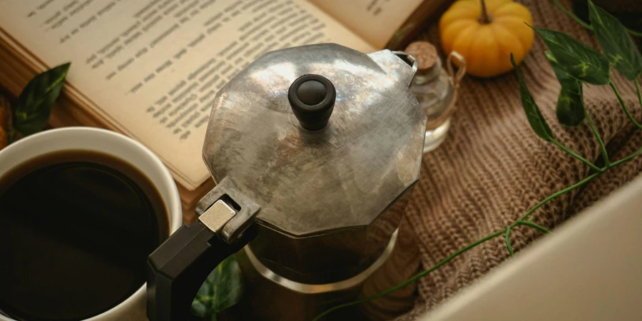 Sebuah pressure cooker di samping secangkir kopi dan sebuah buku terbuka di atas meja kayu