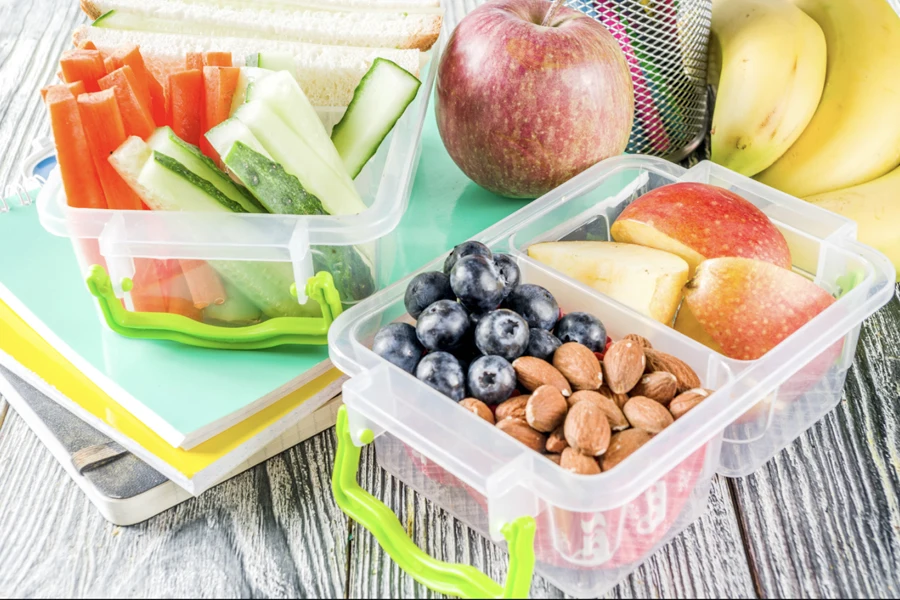 A transparent lunch box containing fruits, veg, and nuts