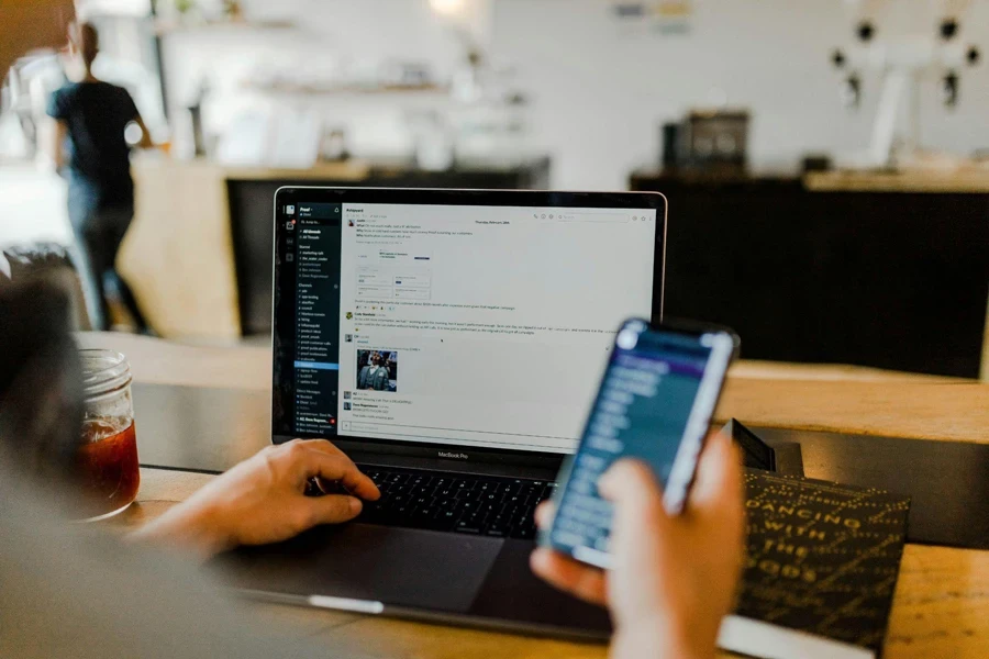 Um indivíduo trabalhando em um laptop, com um telefone celular apoiado na mesa