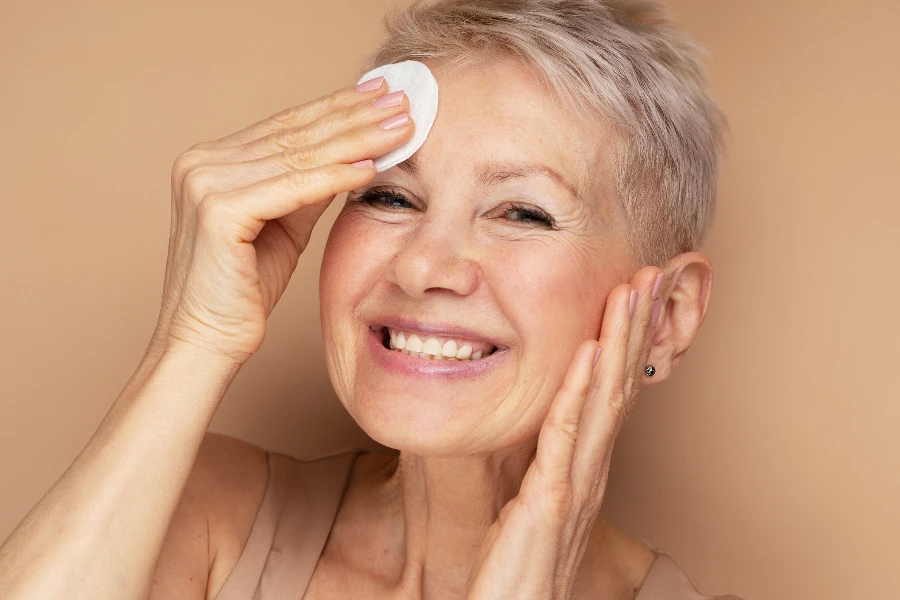 Schöne ältere 60er-Jahre-Frau mit kurzen Haaren erledigt ihre Alltagsroutine und entfernt ihr Make-up mit einem Wattepad