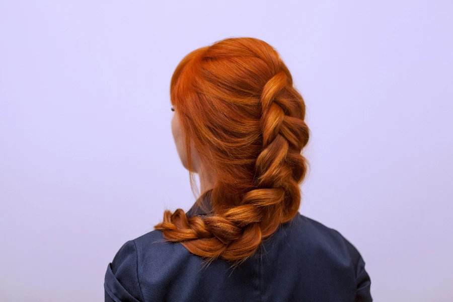 Красивая девушка с длинными рыжими волосами, заплетенными во французскую косу.