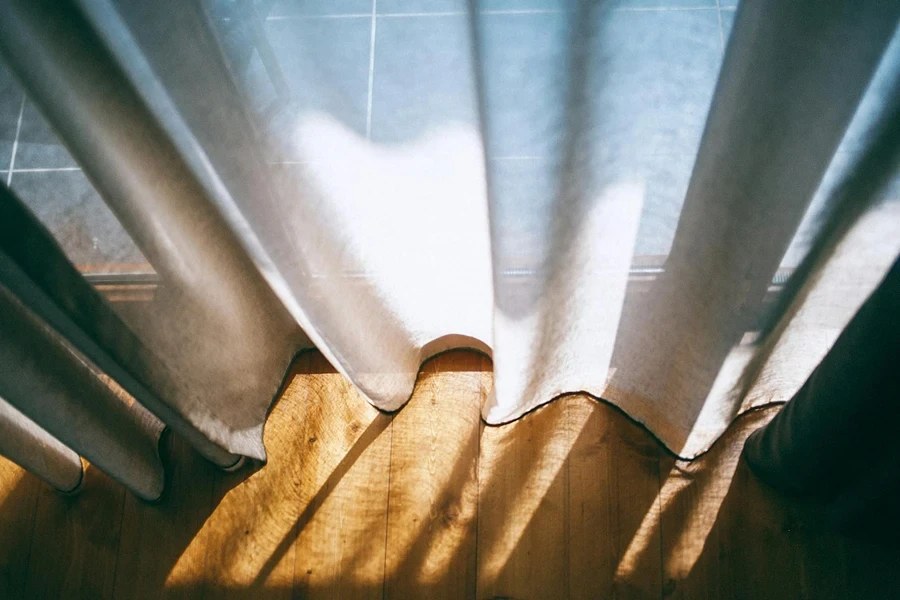 De cima da janela panorâmica com cortinas transparentes iluminadas pela luz do sol no quarto