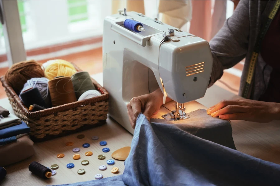 Prise de vue d'en haut d'un créateur de mode méconnaissable utilisant une machine à coudre moderne pour confectionner de jolis vêtements en atelier