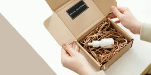 Hands of a Person Opening a Box with a White Bottle