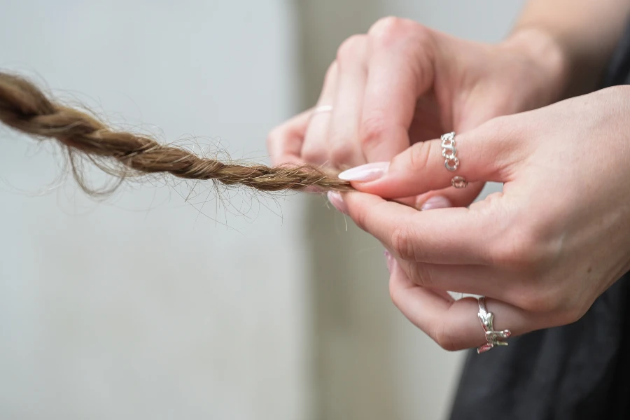 Hands of a young woman with rings and styled nails braiding the hair of a friend