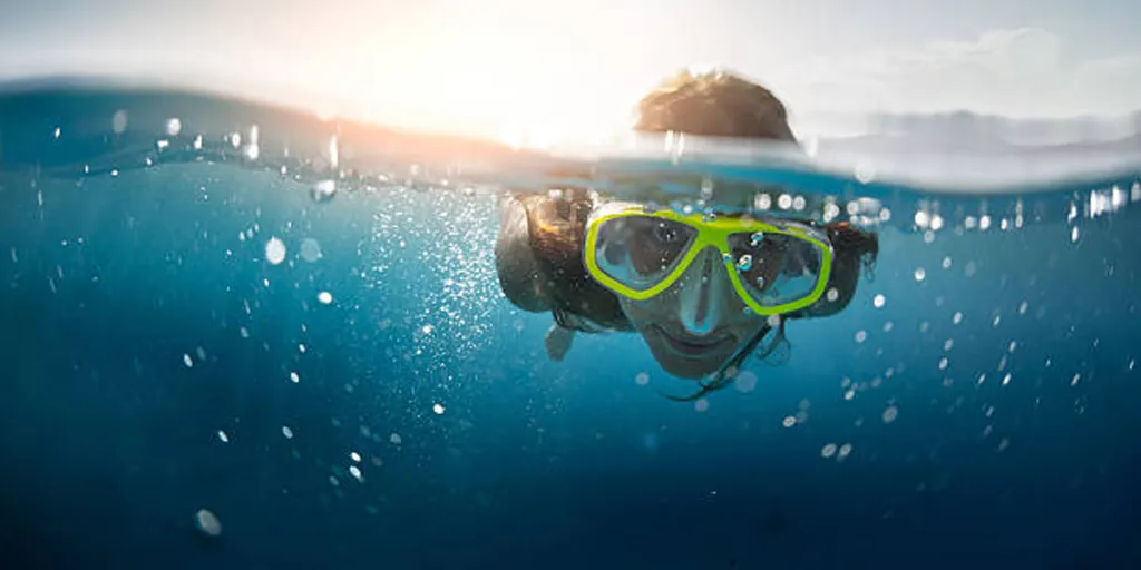 Sarı şnorkel maskesiyle okyanusta yüzen çocuk