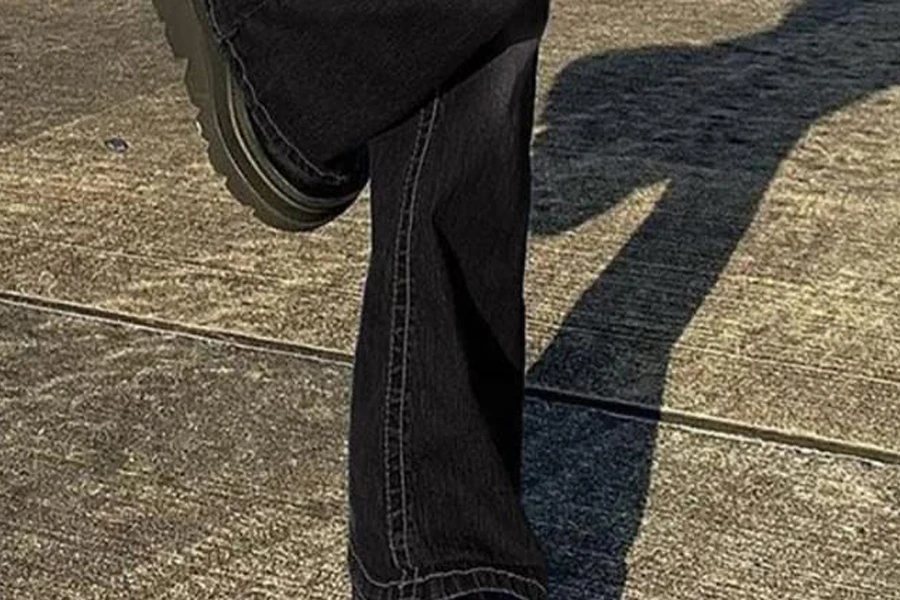 Wanita dengan sepatu bot tebal mengenakan celana jins rendah berkaki lebar berwarna hitam