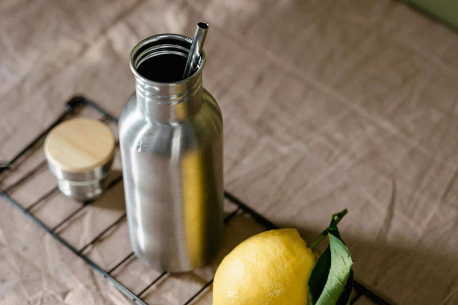 Silberne Isolierflasche mit silbernem Strohhalm und Zitrone