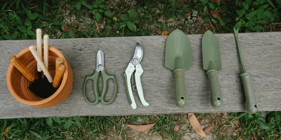 منظر علوي لصف من المقص والمجارف وأدوات لتفكيك التربة بالقرب من وعاء مع أدوات على مقعد خشبي في الحديقة