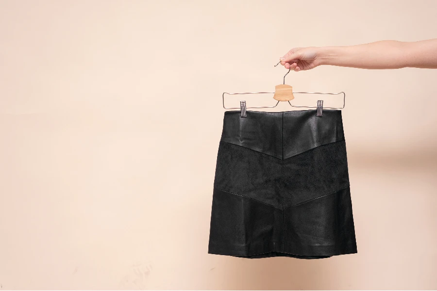 Woman is holding in hand a black skirt on the hanger on the light background