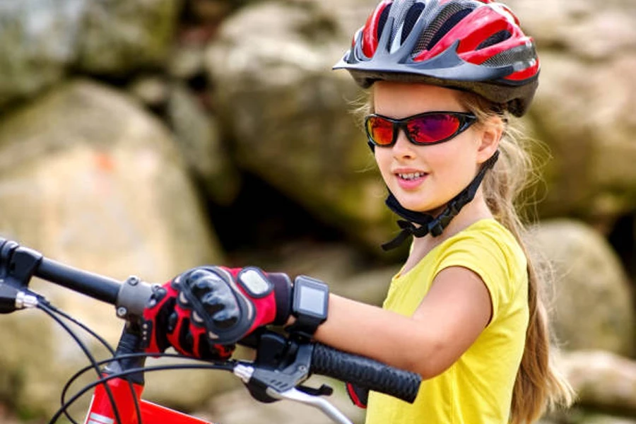فتاة صغيرة ترتدي خوذة حمراء وقفازات ركوب الدراجات