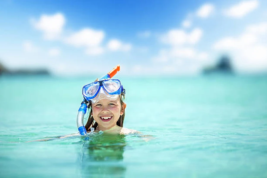 Mavi gözlüklü ve okyanusta şnorkel maskesi olan genç kız