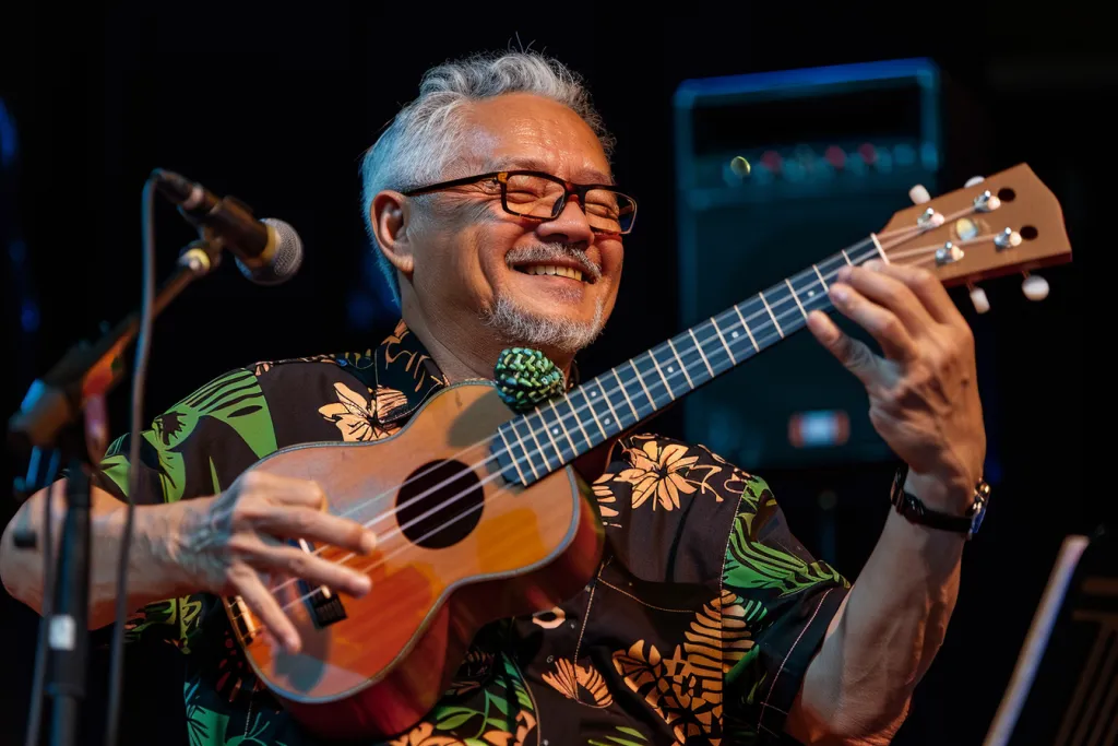 um homem americano na casa dos cinquenta, tocando ukulele no palco