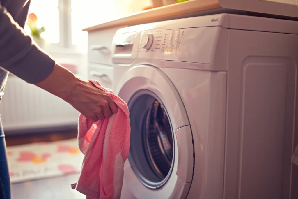 Человек кладет одежду в стиральную машину