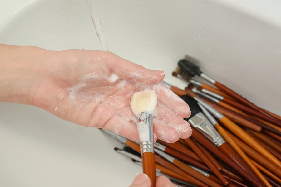 lavare il pennello per il trucco con sapone e schiuma nel lavandino