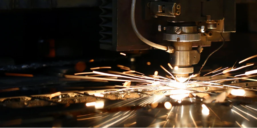 Faíscas voam para fora da cabeça da máquina para processamento de metal a laser em fundo de planta metalúrgica