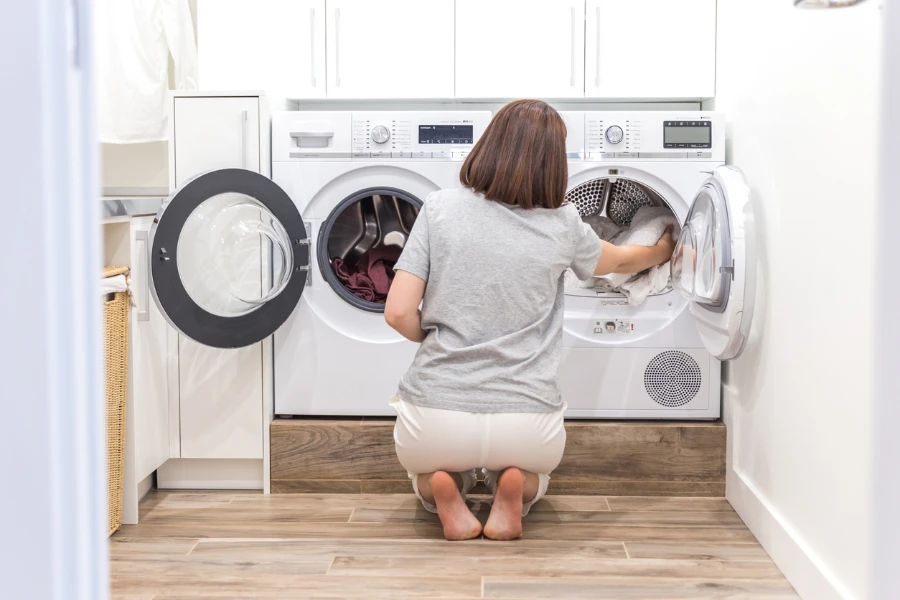 Женщина загружает грязную одежду в стиральную машину для стирки в подсобном помещении