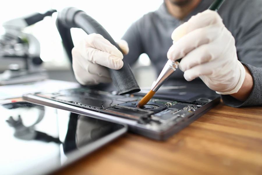 Il chimico maschio con guanti protettivi bianchi utilizza l'aspirapolvere nel servizio di riparazione del laptop