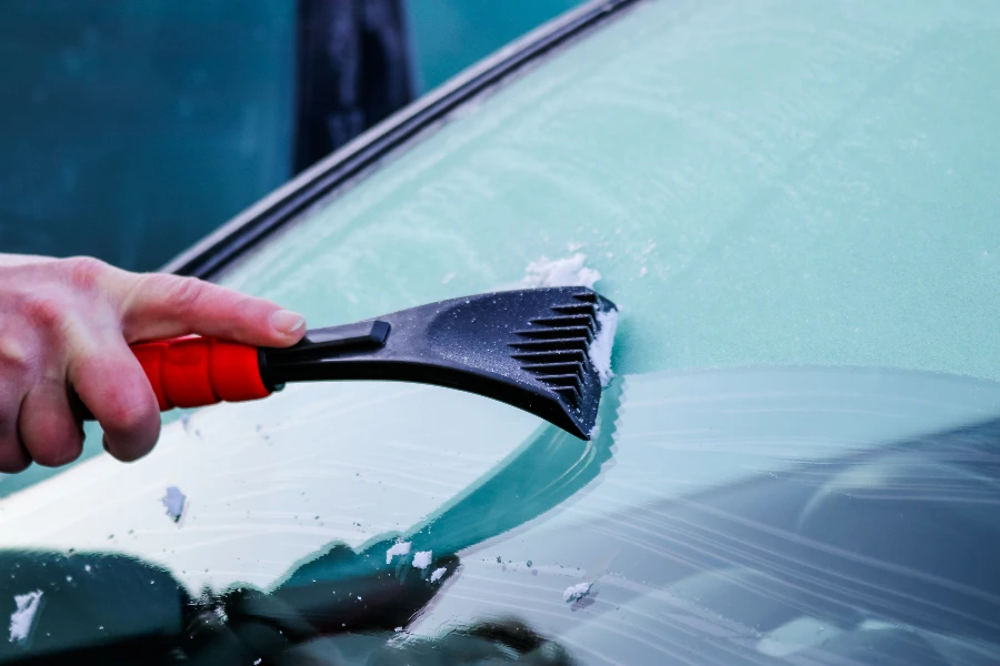 Manusia menggunakan semprotan defroster untuk menghilangkan embun beku dari kaca depan mobil