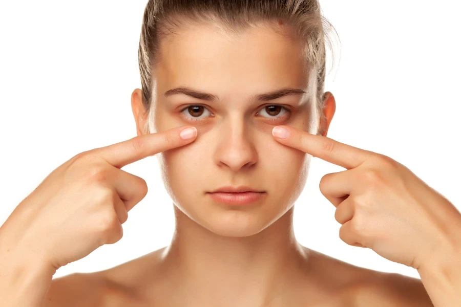 Jeune femme touchant ses paupières basses sur fond blanc