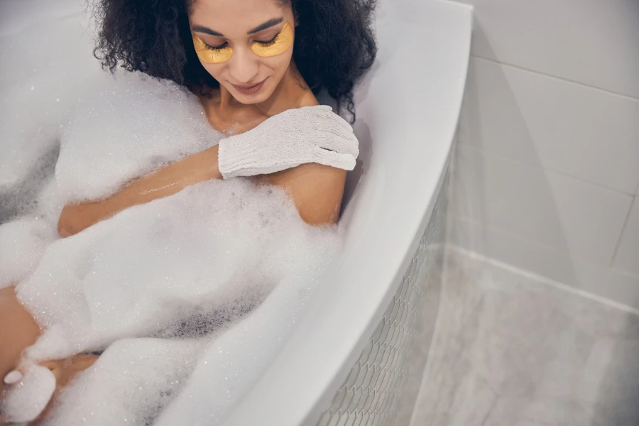 Wanita cantik dengan rambut hitam keriting bersantai di bak mandi selama prosedur kecantikan di rumah