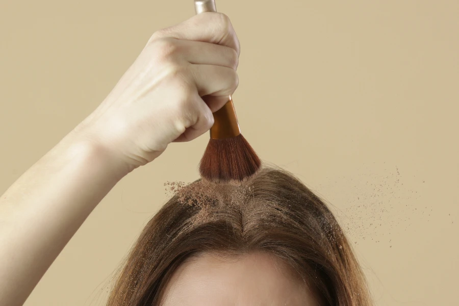 Nahaufnahme einer Frau, die natürliches Trockenshampoo auf die Haarwurzeln aufträgt
