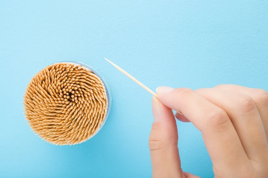 Young woman fingers holding sharp wooden toothpick
