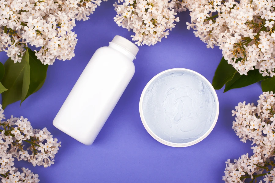 cosméticos em frascos brancos sobre um fundo roxo com ramos de vista superior lilás branco