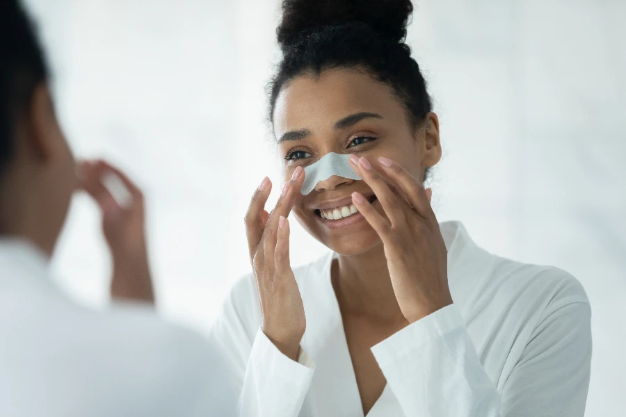 Mirror reflection close up smiling African American young woman applying anti blackhead patch