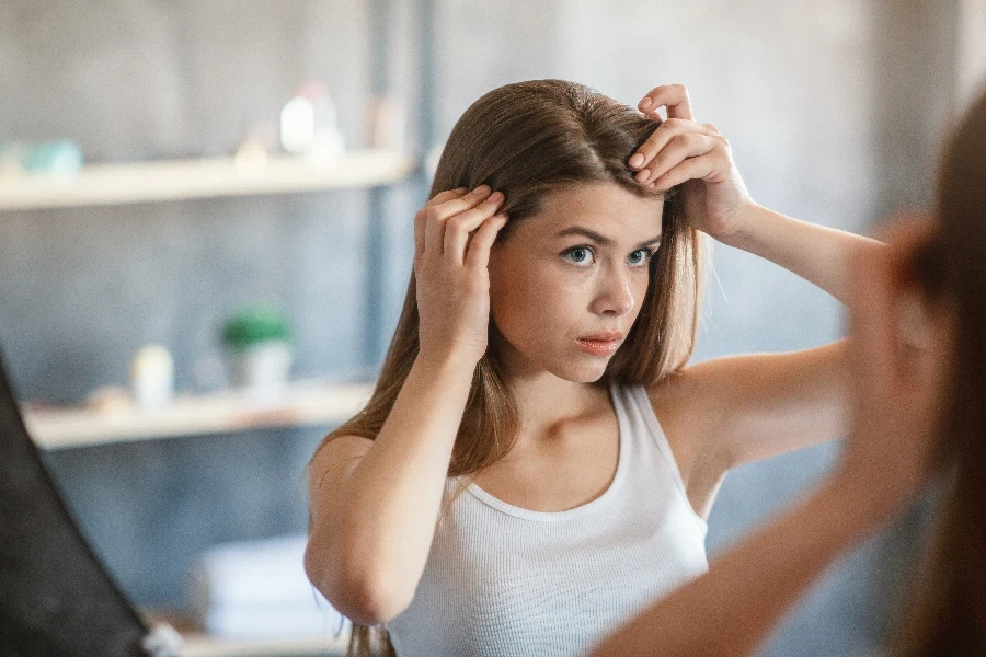 Ragazza millenaria con problemi di perdita di capelli che si guarda allo specchio a casa