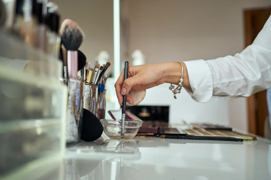 Визажист выбирает продукты и кисточку на своем косметическом столе в своей современной студии макияжа