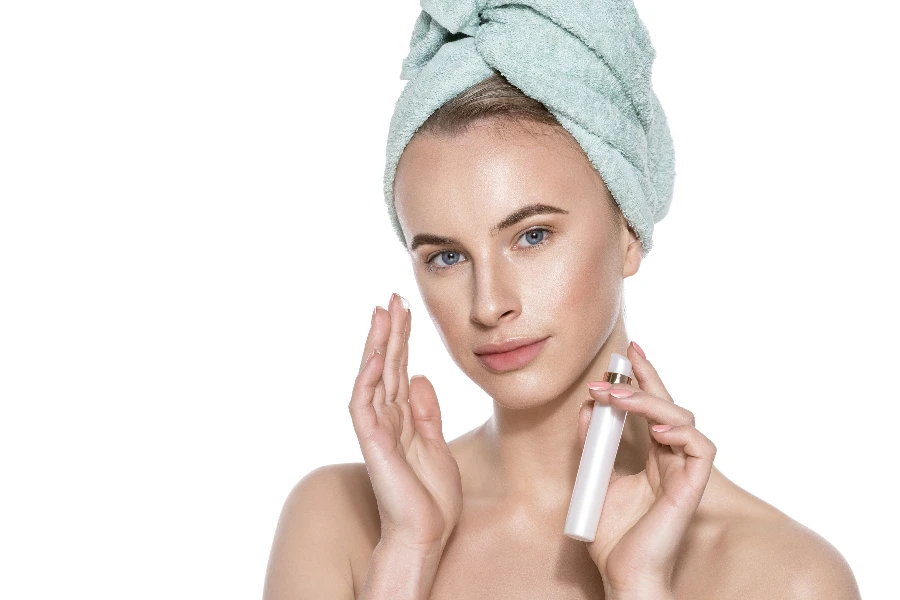 Beautiful young woman wearing head towel using natural moisturizer
