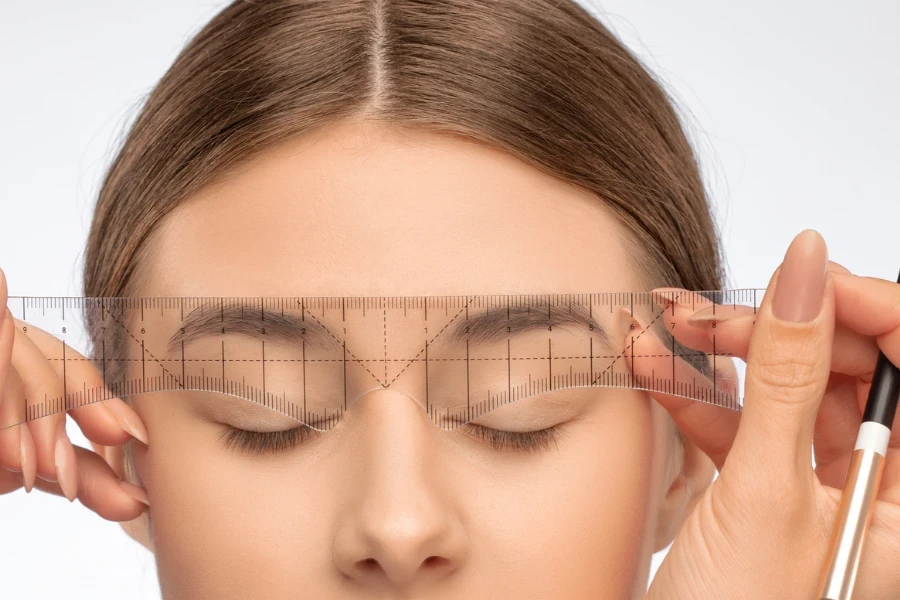 Make-up artist makes markings with white pencil for eyebrow and paints eyebrows
