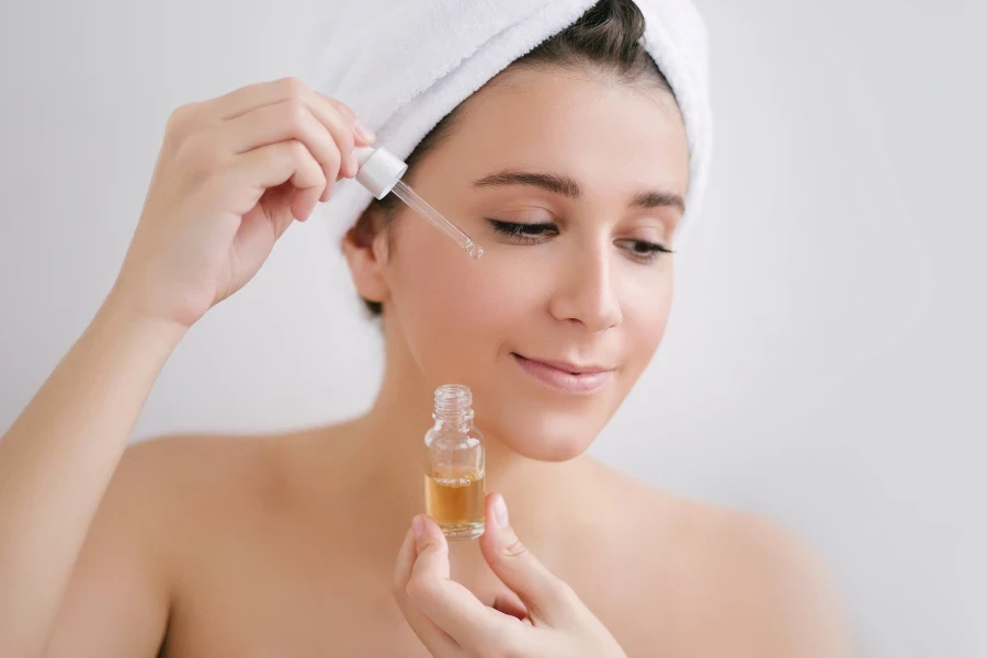 Retrato de una hermosa mujer joven con una toalla en la cabeza sosteniendo aceite facial