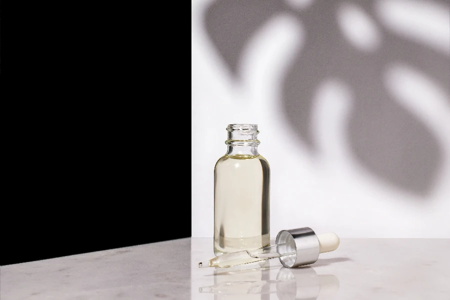 A glass dropper bottle with an eyedropper on a background with a shadow of tropical leaves