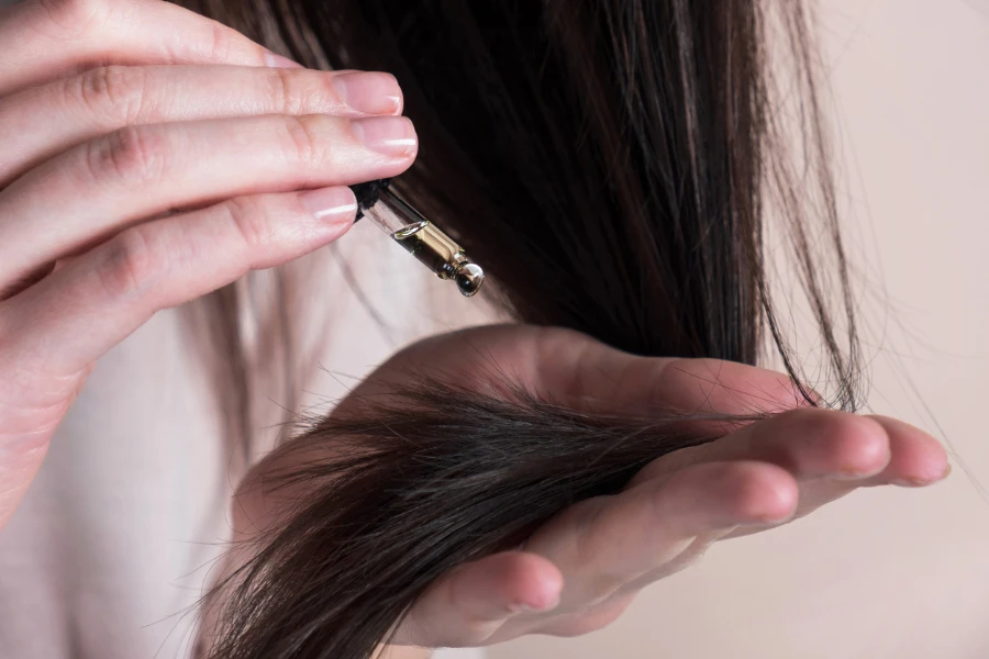 Mulher aplicando conta-gotas com essência de óleo ou soro nas pontas do cabelo