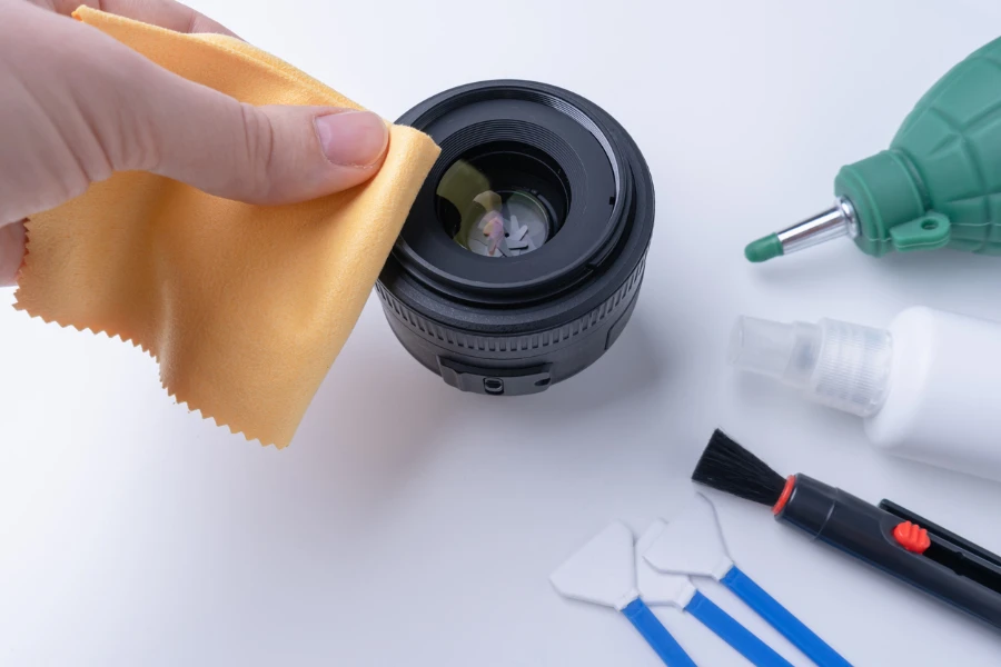 La mano del fotografo con microfibra gialla pulisce l'obiettivo della fotocamera