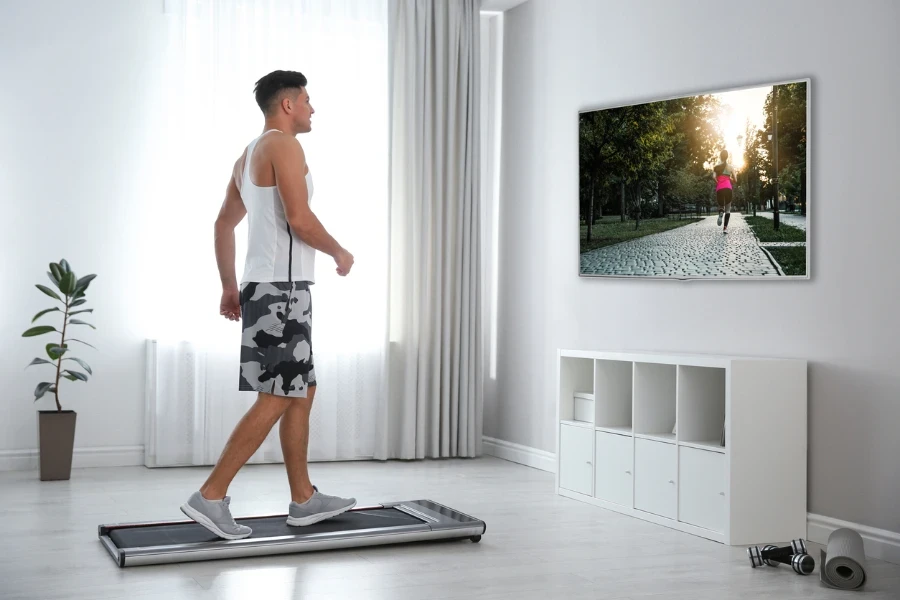 Uomo sportivo che si allena sul tapis roulant e guarda la TV a casa