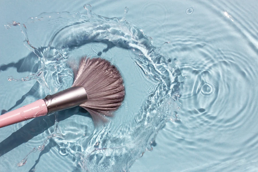 Pincel de maquillaje en agua limpia con un chorrito. Concepto de cosmética de verano.