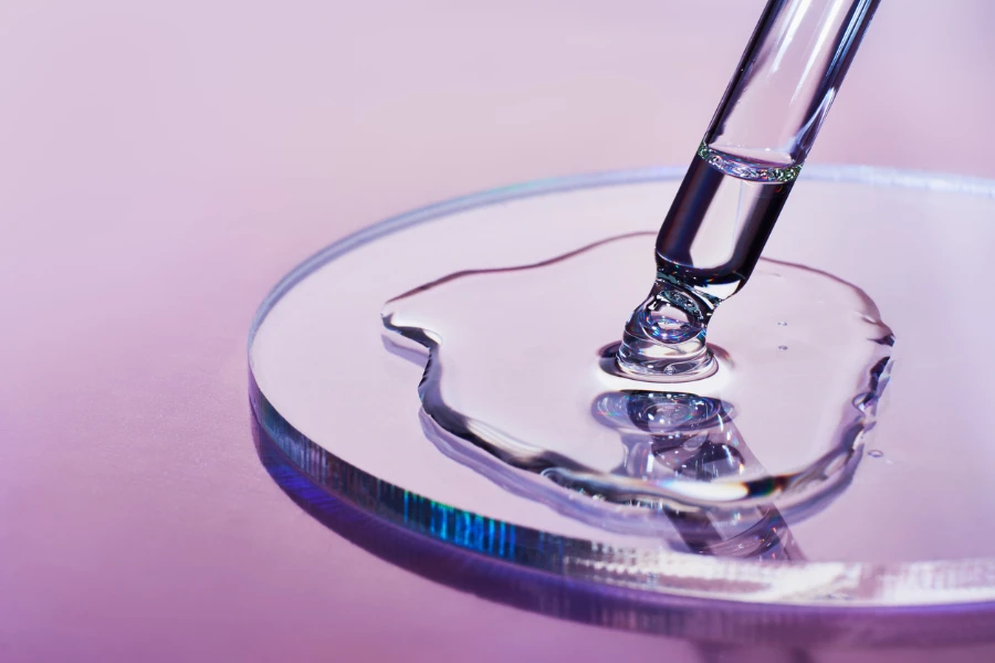 Pipetta con campione di prodotto cosmetico in capsula Petri su sfondo olografico
