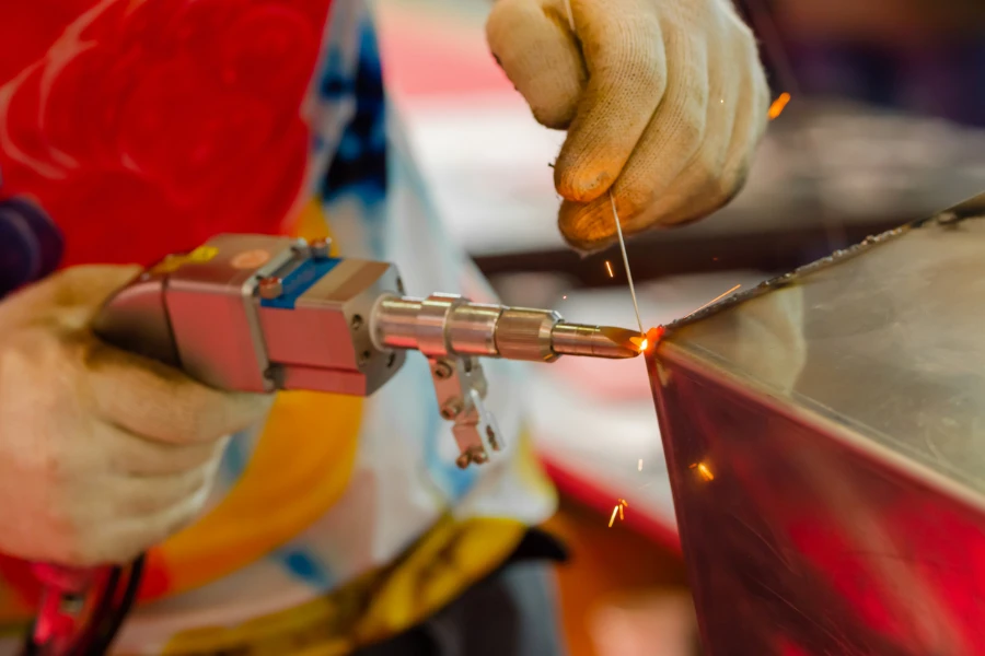 Mãos de soldador usando máquina de solda a laser portátil com faíscas