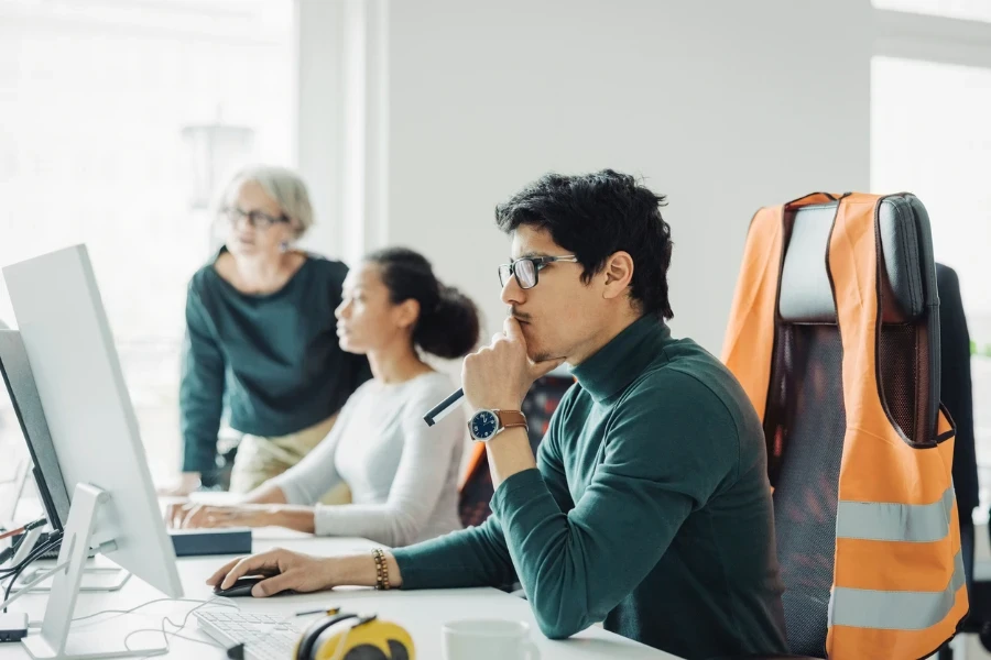 Junger männlicher Architekt sitzt an seinem Schreibtisch und arbeitet am Computer