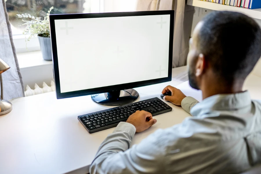 Ev ofisindeki bilgisayar monitörünün beyaz ekranı üzerinde çalışan adam