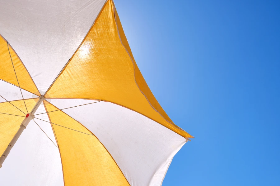 paraguas amarillo y blanco sobre un cielo azul para protegerse del sol en la playa